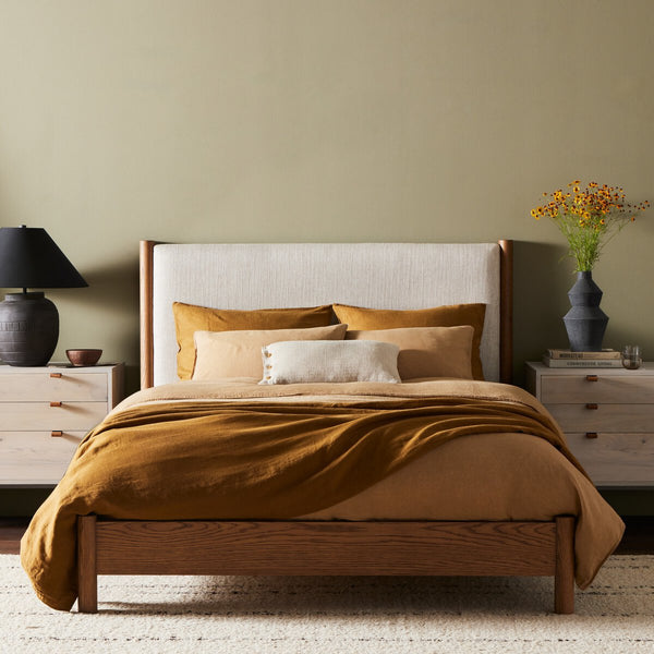 Cama moderna tapizada con estructura de madera maciza y cabecero alto de lino.