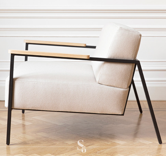 Sillón moderno con estructura de metal negro, reposabrazos de madera natural y tapizado gris claro.