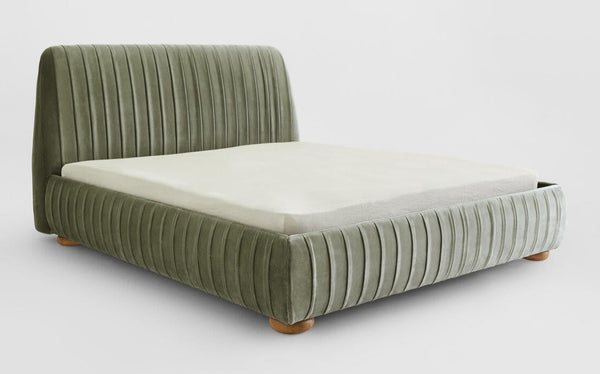 Cama moderna de terciopelo capitoné con plataforma tapizada en verde salvia y patas redondeadas de madera.