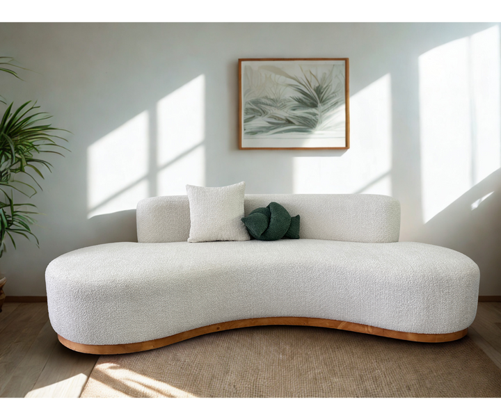 Modern white sofa with a wooden base in a bright room with sunlight streaming through windows.