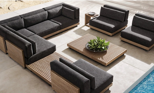 Moderno sofá seccional de teca para exterior: asientos profundos con base de listones de madera y cojines color carbón.