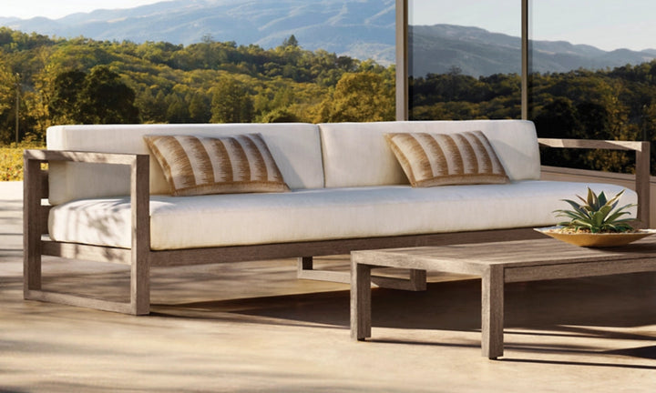 Outdoor furniture set with wooden frames and white cushions on a patio with scenic view.