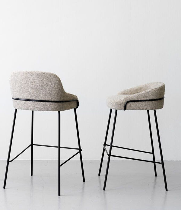 Taburete de bar moderno tapizado en bouclé, con respaldo curvo y estructura de metal negro.